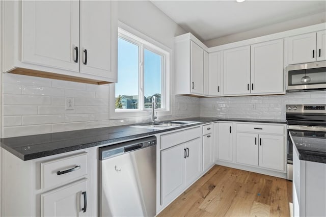 kitchen featuring stainless steel appliances, a sink, white cabinetry, light wood-style flooring, and backsplash