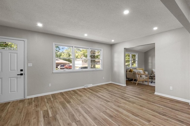 unfurnished living room with wood finished floors, a textured ceiling, recessed lighting, and baseboards