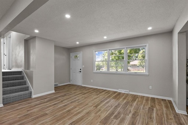 entryway featuring a textured ceiling, recessed lighting, wood finished floors, stairs, and baseboards