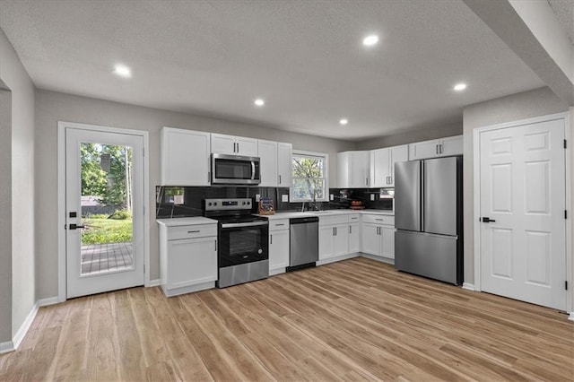 kitchen with stainless steel appliances, tasteful backsplash, white cabinetry, light countertops, and light wood finished floors