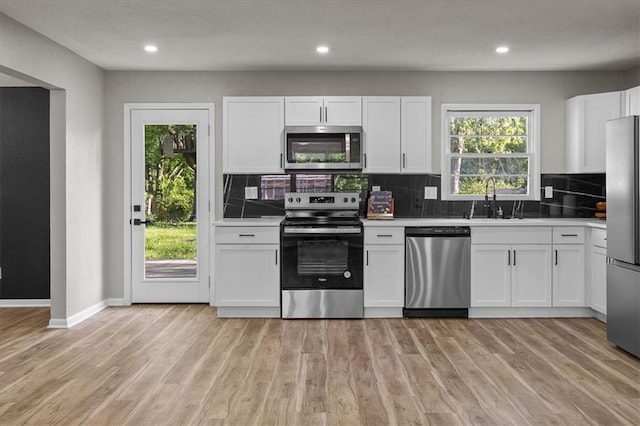 kitchen featuring stainless steel appliances, a sink, tasteful backsplash, white cabinets, and light wood-type flooring