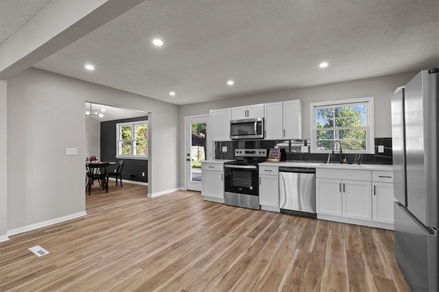 kitchen with stainless steel appliances, a sink, a textured ceiling, light wood-style flooring, and plenty of natural light