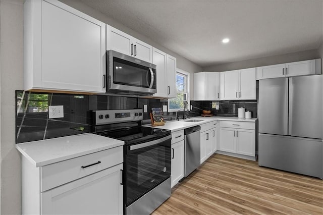 kitchen featuring stainless steel appliances, a sink, light wood-style flooring, white cabinetry, and backsplash
