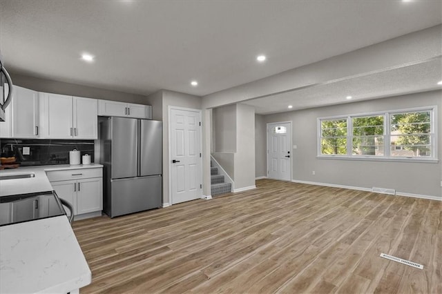 kitchen with freestanding refrigerator, white cabinets, decorative backsplash, light wood finished floors, and recessed lighting