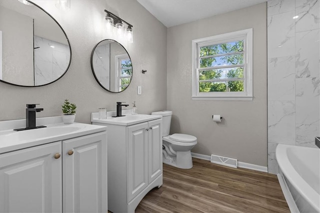 full bathroom featuring two vanities, a tub, toilet, wood finished floors, and baseboards