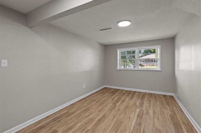 spare room with light wood-style flooring, a textured ceiling, and baseboards