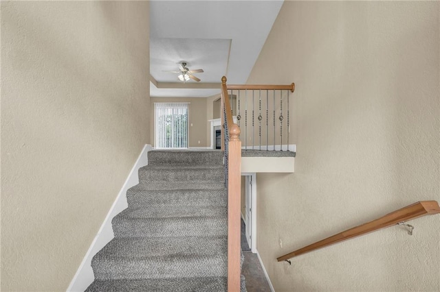 staircase with a ceiling fan, a textured wall, and baseboards
