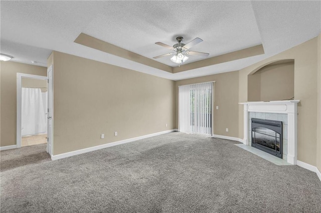 unfurnished living room featuring a raised ceiling, a textured ceiling, a ceiling fan, carpet flooring, and baseboards