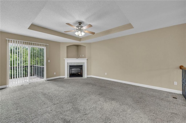 unfurnished living room with a tray ceiling, baseboards, ceiling fan, a textured ceiling, and carpet flooring