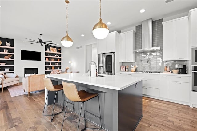 15932 W 171st Ter, Olathe, KS 66062 - kitchen with wall chimney exhaust hood, appliances with stainless steel finishes, recessed lighting, a kitchen island with sink, and light wood finished floors