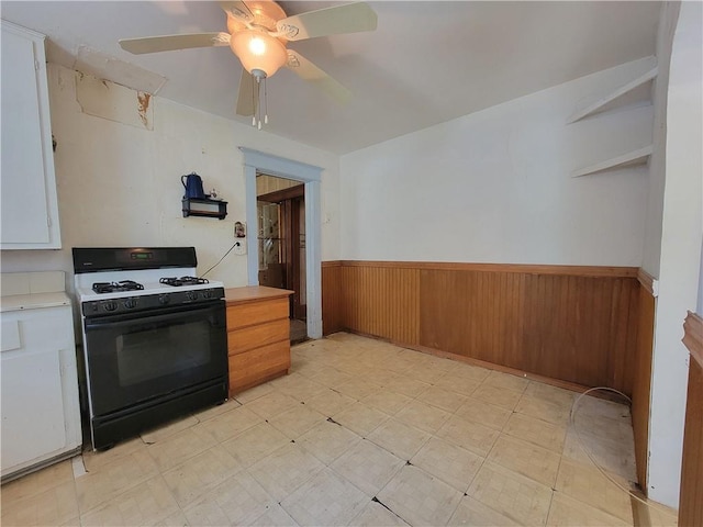 111 S Wall St, Leeton, MO 64761 - kitchen with range with gas cooktop, wainscoting, light countertops, a ceiling fan, and wood walls