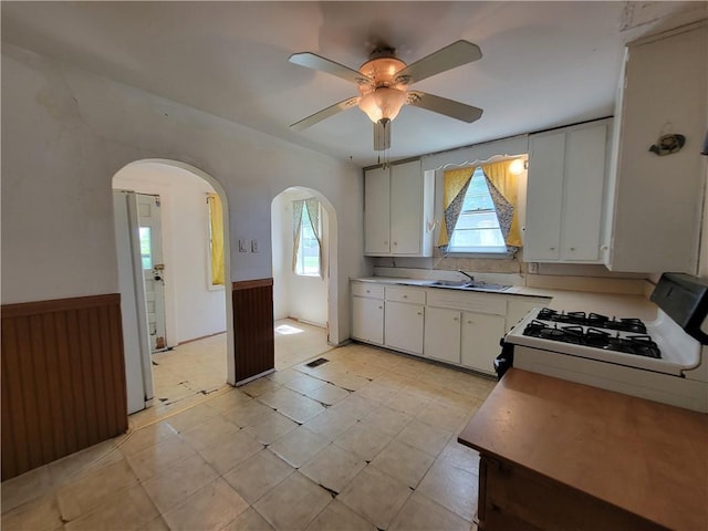 111 S Wall St, Leeton, MO 64761 - kitchen featuring white gas range, arched walkways, a wainscoted wall, ceiling fan, and white cabinets