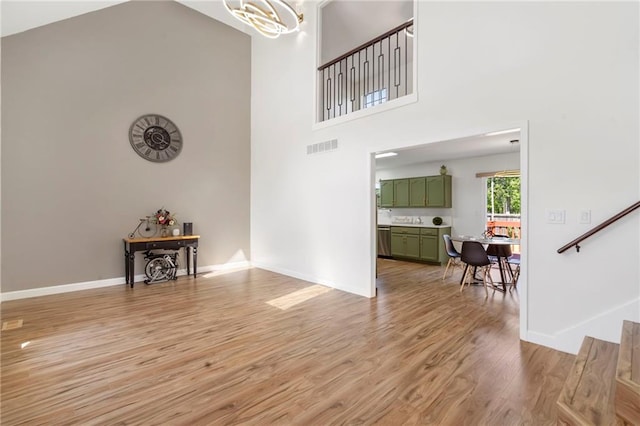 entryway with a towering ceiling, light wood finished floors, baseboards, a chandelier, and stairs