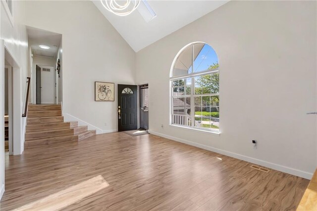 foyer featuring high vaulted ceiling, light wood-style floors, stairs, and baseboards