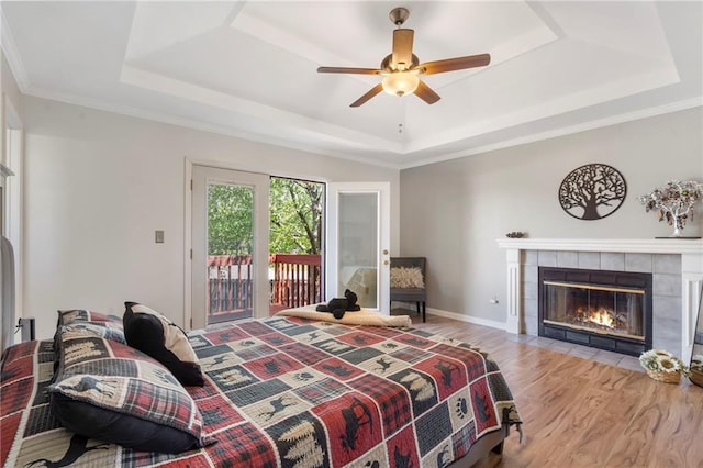 bedroom featuring a tray ceiling, access to exterior, wood finished floors, and a tile fireplace
