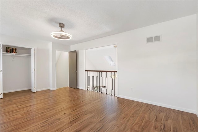 unfurnished bedroom with wood finished floors, baseboards, a textured ceiling, and a closet
