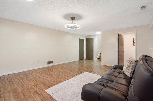 living room featuring stairs, light wood-type flooring, baseboards, and a textured ceiling