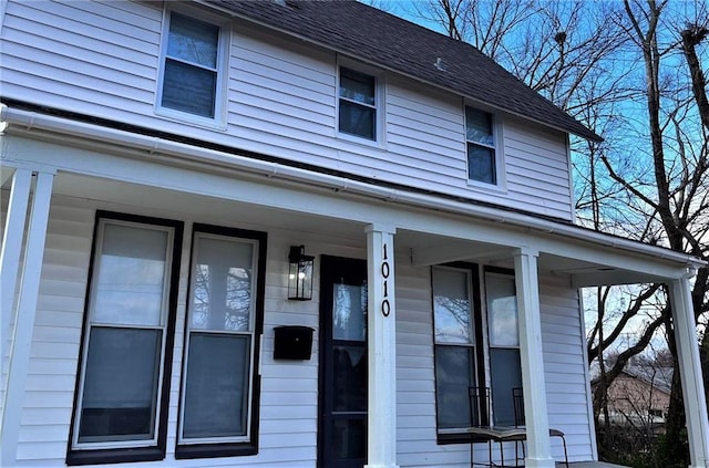 doorway to property featuring a porch and a shingled roof