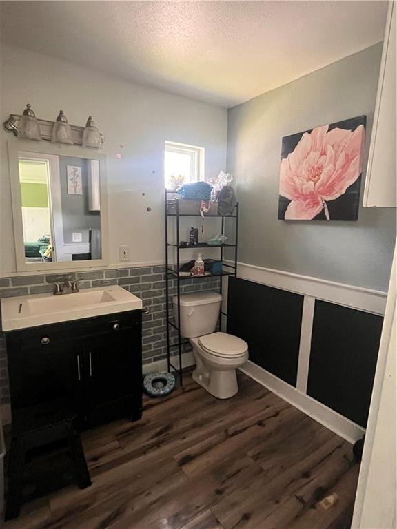 half bath with toilet, a wainscoted wall, wood finished floors, a textured ceiling, and vanity