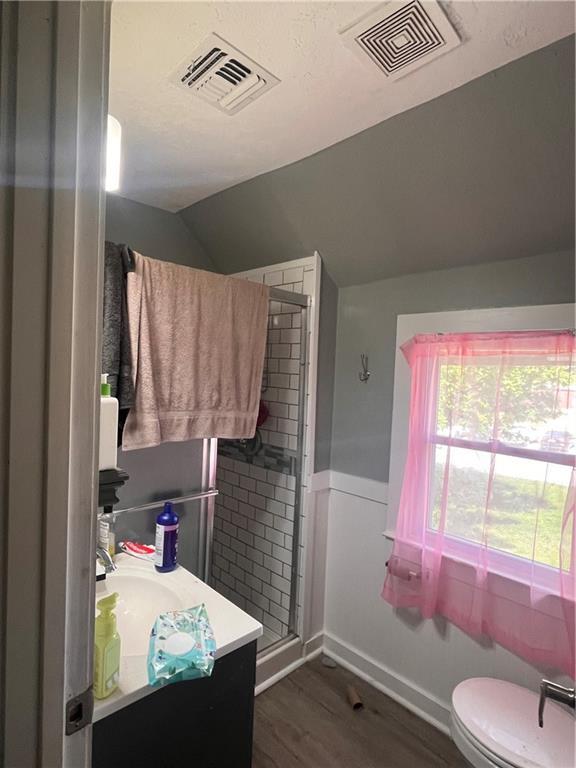 full bath featuring wood finished floors, vaulted ceiling, vanity, toilet, and a shower stall