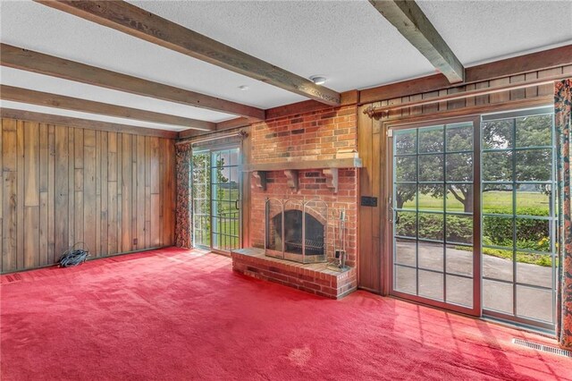28210 Hedge Ln, Paola, KS 66071 - unfurnished living room featuring wood walls, beam ceiling, a textured ceiling, carpet, and a brick fireplace