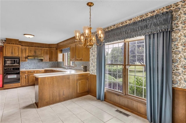 28210 Hedge Ln, Paola, KS 66071 - kitchen featuring black appliances, under cabinet range hood, a chandelier, a peninsula, and brown cabinetry