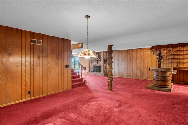 28210 Hedge Ln, Paola, KS 66071 - unfurnished living room featuring stairs, wood walls, carpet flooring, a brick fireplace, and a textured ceiling