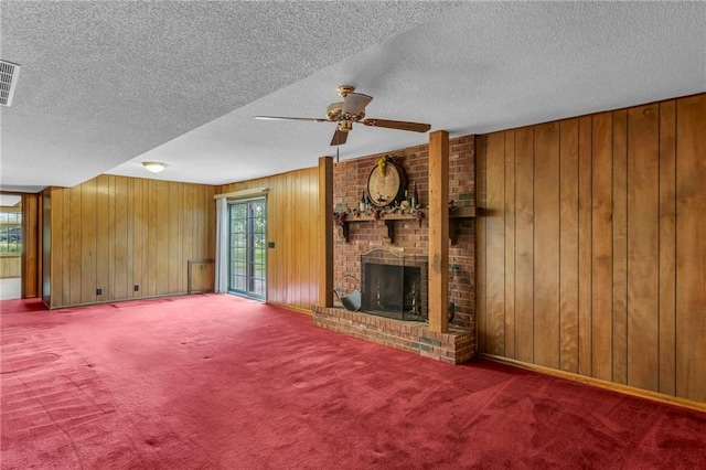28210 Hedge Ln, Paola, KS 66071 - unfurnished living room with a ceiling fan, wooden walls, carpet flooring, a fireplace, and a textured ceiling