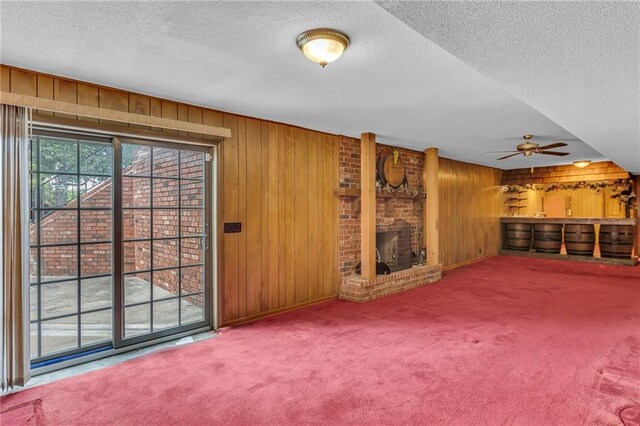 28210 Hedge Ln, Paola, KS 66071 - unfurnished living room featuring a textured ceiling, wooden walls, carpet, a fireplace, and a ceiling fan