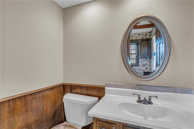28210 Hedge Ln, Paola, KS 66071 - half bathroom featuring a wainscoted wall, vanity, toilet, and wooden walls