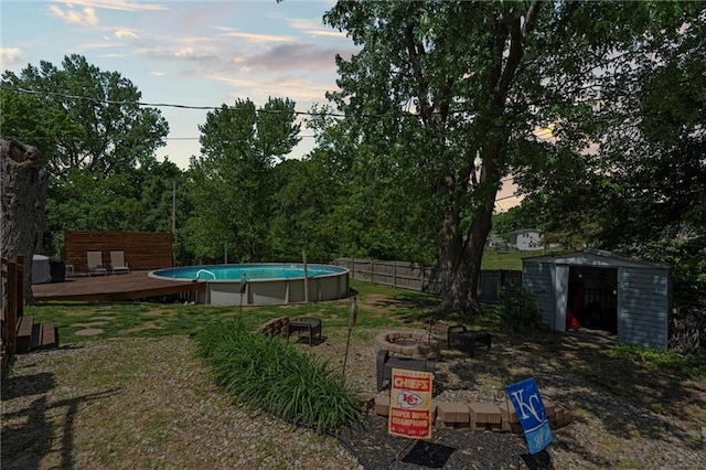 view of yard featuring a fire pit, a shed, a wooden deck, an outdoor pool, and an outbuilding