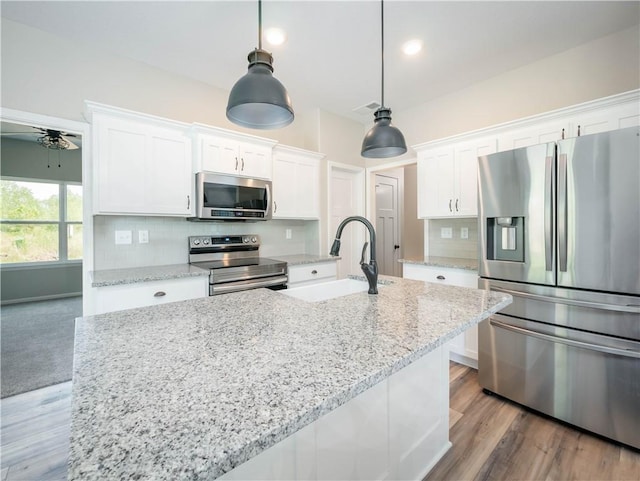 1313 N White Oaks Ln, Oak Grove, MO 64075 - kitchen featuring stainless steel appliances, a sink, white cabinetry, backsplash, and a kitchen island with sink
