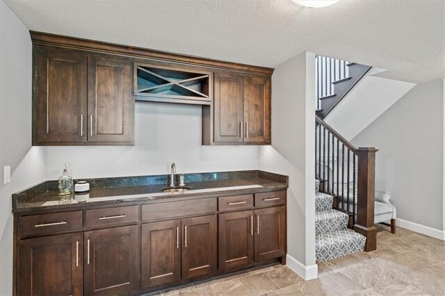 16456 Cody St, Overland Park, KS 66062 - kitchen featuring a sink, dark stone countertops, dark brown cabinetry, a textured ceiling, and baseboards