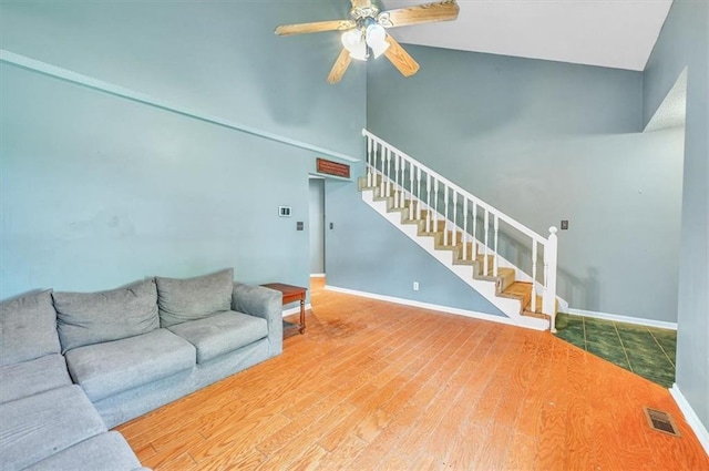living room featuring stairway, ceiling fan, baseboards, wood finished floors, and high vaulted ceiling