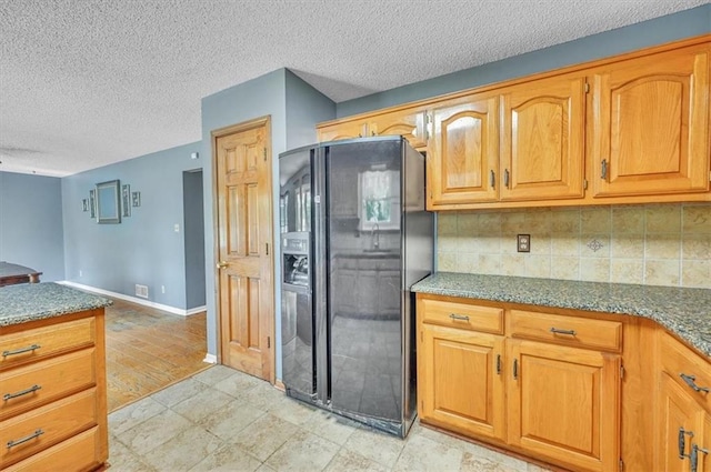 kitchen with black fridge, decorative backsplash, a textured ceiling, dark stone counters, and baseboards
