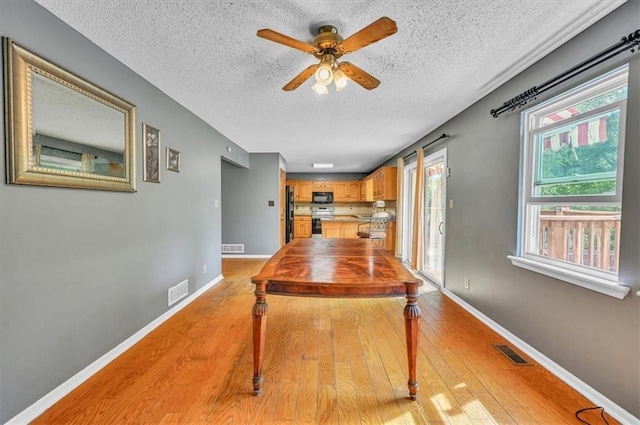 dining space with a textured ceiling, light wood-style flooring, a ceiling fan, and baseboards