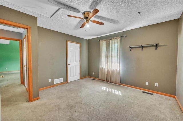 unfurnished bedroom featuring attic access, carpet flooring, baseboards, a textured ceiling, and a ceiling fan