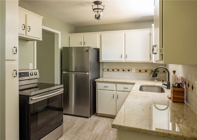 kitchen with stainless steel appliances, a sink, decorative backsplash, light stone countertops, and white cabinets