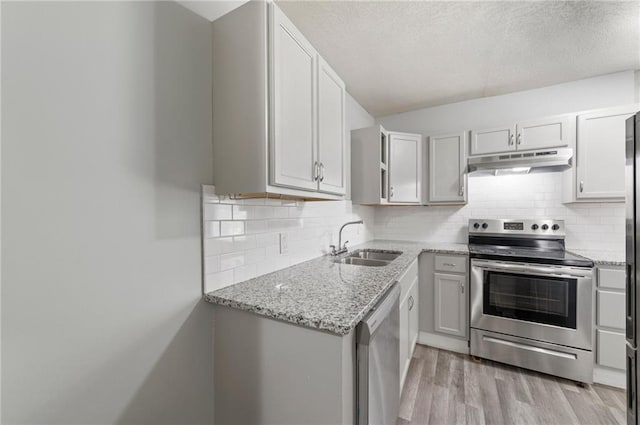 kitchen featuring stainless steel appliances, under cabinet range hood, a sink, a textured ceiling, and light stone countertops