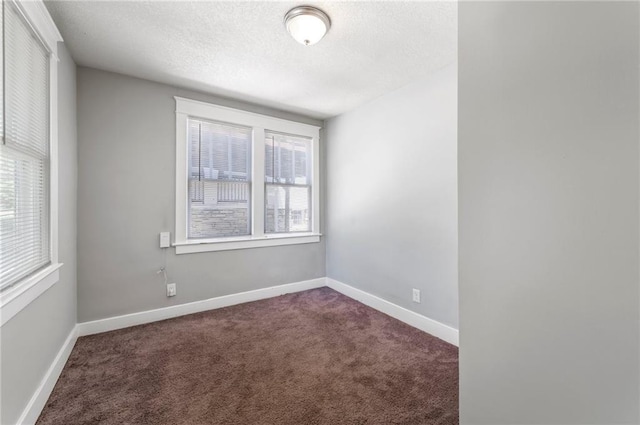 spare room with dark carpet, a textured ceiling, and baseboards