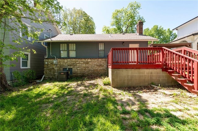 rear view of house with stone siding, a deck, a chimney, and a lawn