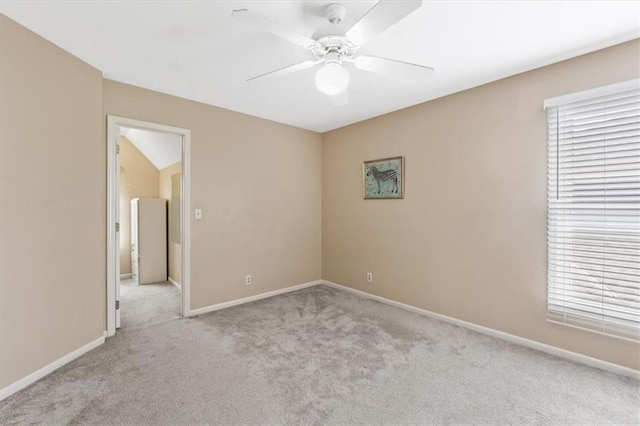 spare room featuring light colored carpet, a ceiling fan, and baseboards