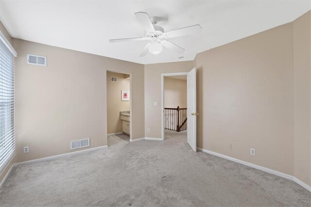 unfurnished bedroom featuring light carpet, baseboards, ceiling fan, and ensuite bathroom
