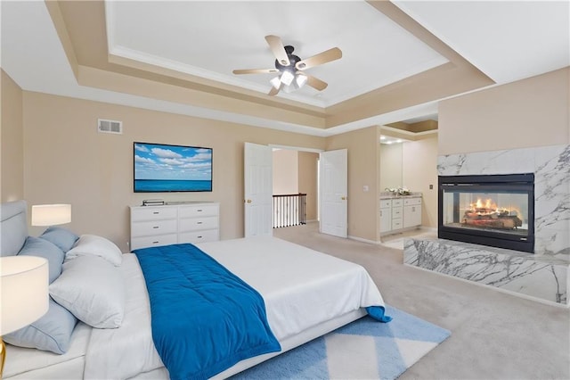 bedroom with a raised ceiling, light carpet, a fireplace, and baseboards