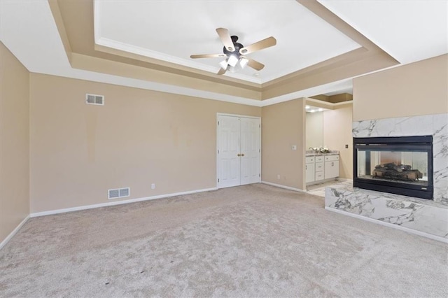 unfurnished living room with a raised ceiling, light carpet, a ceiling fan, a fireplace, and baseboards