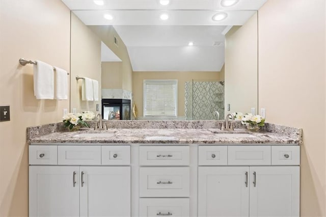 bathroom featuring tiled shower, lofted ceiling, double vanity, and recessed lighting