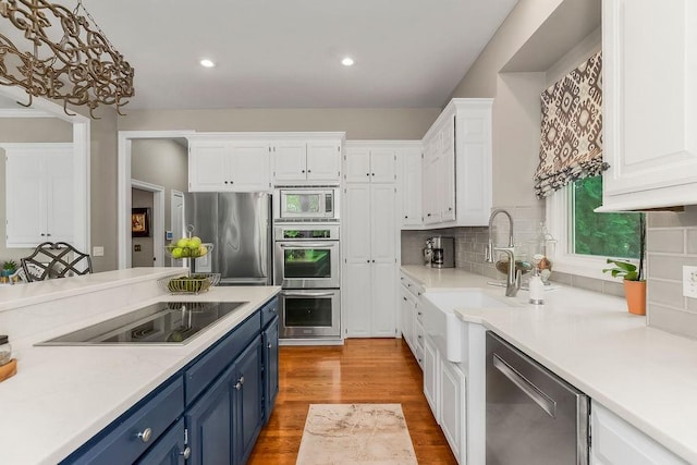 6104 W 144th St, Overland Park, KS 66223 - kitchen with blue cabinets, appliances with stainless steel finishes, white cabinets, a sink, and recessed lighting