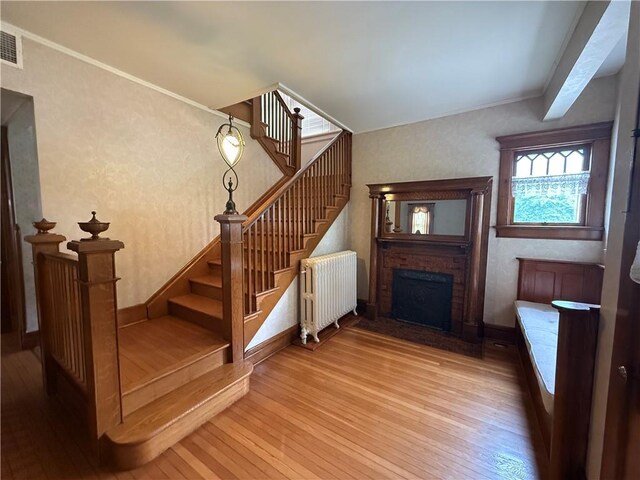 1701 Main St, Lexington, MO 64067 - staircase with radiator heating unit, wood-type flooring, wallpapered walls, a fireplace with flush hearth, and ornamental molding