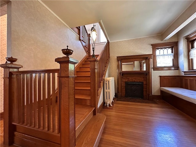 1701 Main St, Lexington, MO 64067 - staircase featuring radiator heating unit, hardwood / wood-style floors, a brick fireplace, crown molding, and wallpapered walls
