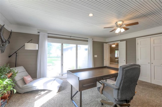 carpeted home office featuring a ceiling fan and wooden walls